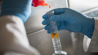 Image of chemistry experiment, adding a yellow liquid to a vial of clear liquid. 